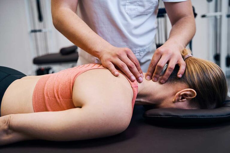 Adult seated at a home workstation adjusting a monitor while gently stretching the neck and shoulders.